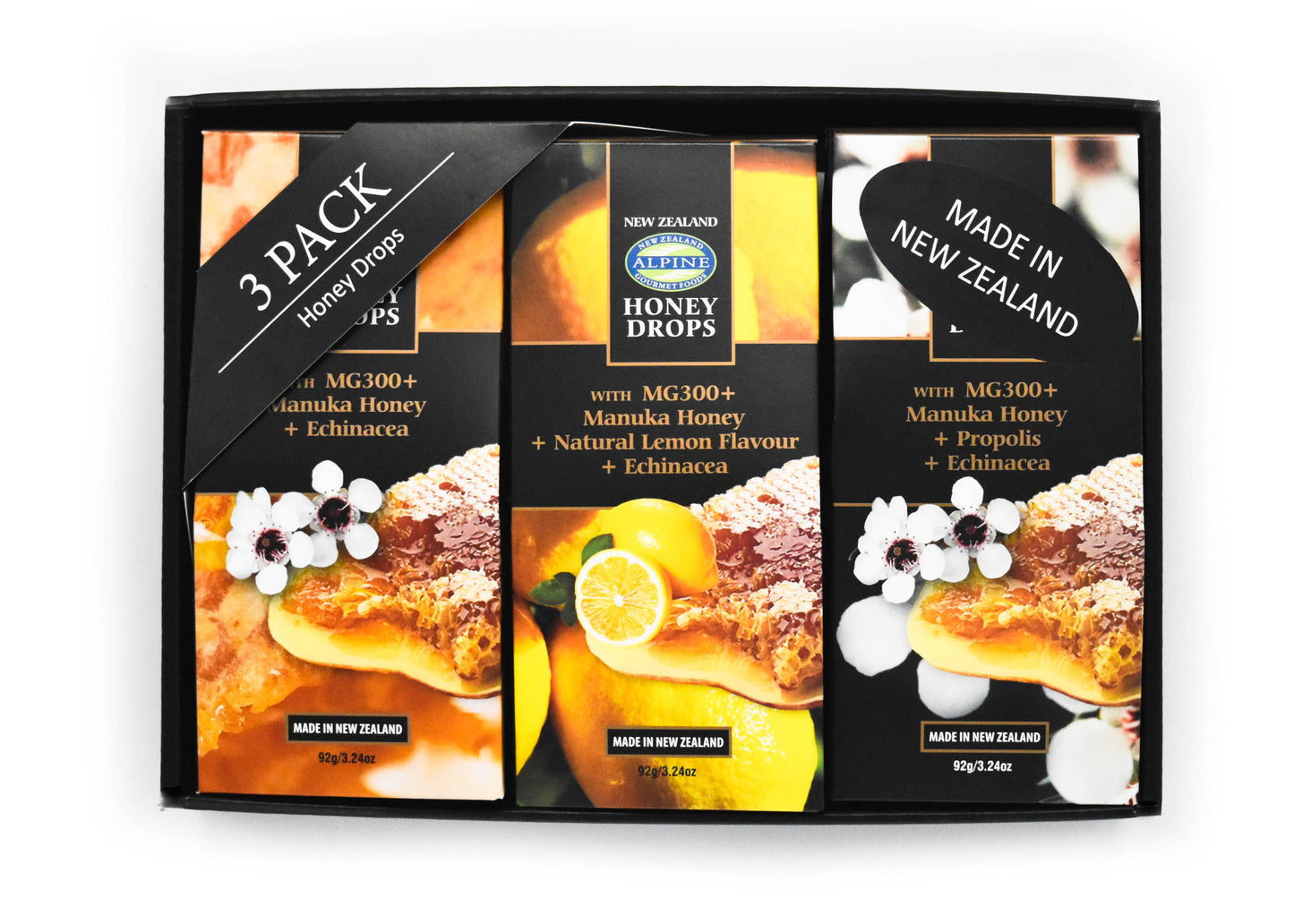 Giftbox on white backdrop. Black gift box with three honey drop pouches. from left to right Manuka Honey plain, Lemon, and then propolis. the images on each pouch align with the flavour. there is also a 3 pack honey drops label in the top left corner and in the right top corner there is a made in New Zealand sticker. 