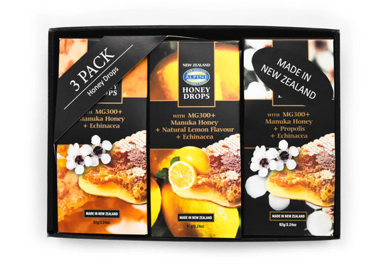 Giftbox on white backdrop. Black gift box with three honey drop pouches. from left to right Manuka Honey plain, Lemon, and then propolis. the images on each pouch align with the flavour. there is also a 3 pack honey drops label in the top left corner and in the right top corner there is a made in New Zealand sticker. 