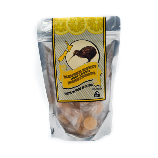 A pouch of Mānka Honey Drops with lemon flavour, individually wrapped, shown in a clear plastic packaging with a yellow label featuring a kiwi bird, map of NZ and lemon slice graphics.