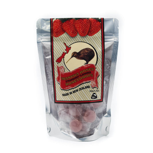 A pouch of Mānka Honey Drops in Strawberry flavor, with the product visibly contained within the clear packaging. The label shows the Mānka Honey brand logo, a kiwi bird, and strawberries, indicating the flavor.