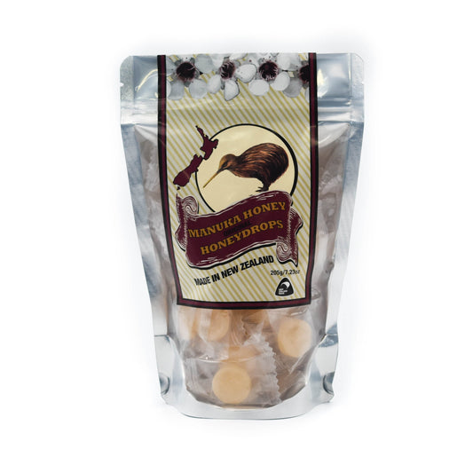 Manuka Honey drops in a clear pouch where you can see individually wrapped honey drops. The label has manuka flowers, a map of NZ and a kiwi bird. 